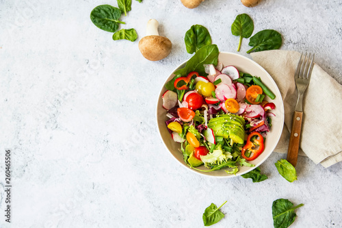 Healthy salad with bio organic vegetables, green vegan meal with avocado, pepper, radish, tomatoes, lettuce, cabbage, spring colorful salad closeup, clean eating concept top view photo