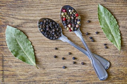 Spice mix and peppercorns in metal spoons and dried bay leafs on old wooden background. Set of spices. Closeup. Selective focus. Top view.