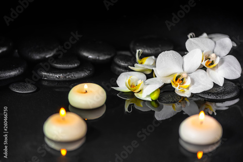 spa concept of white orchid (phalaenopsis), candles and black zen stones with drops on water with reflection
