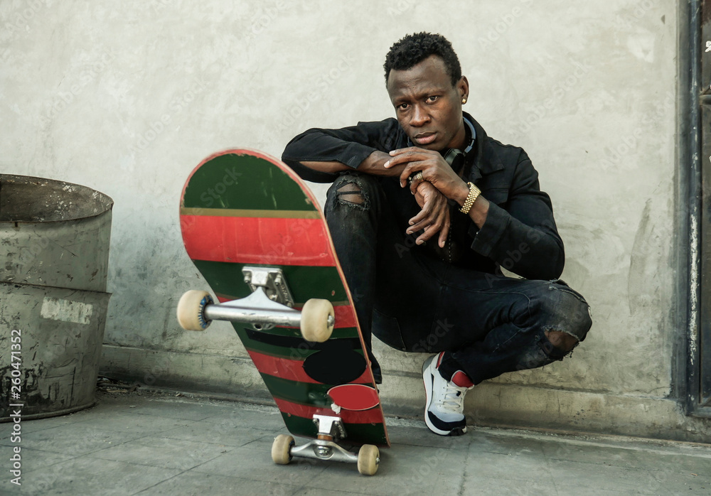 urban portrait of young attractive and serious black afro American man with skate  board squatting on street corner looking cool posing in badass bad boy  attitude Stock Photo | Adobe Stock