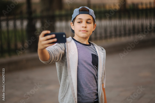 Young boy make a selfie on smartphone in the centre of the city. Cute boy in blue hat. Stylish school boy