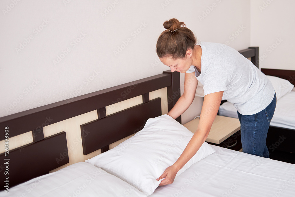 Beautiful young woman corrected pillow on bed at home or in hotel room, copy space Beautiful young woman corrected pillow on bed at home or in hotel room, copy space