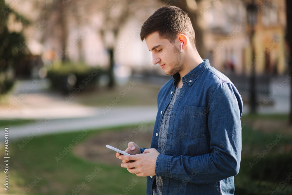 Young man use phone and wireless headphones and print message in social network Young man use phone and wireless headphones and print message in social network