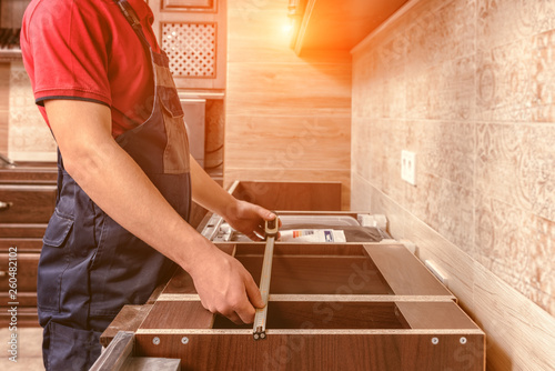 A young worker is assembling modern wooden kitchen furniture.