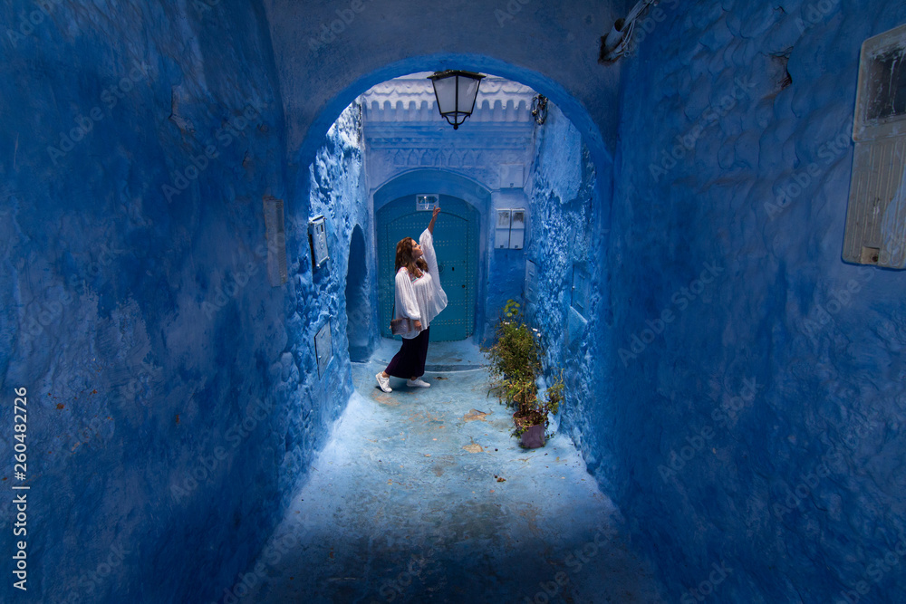 A young woman strolls through the streets of Chefchaouen, the blue town in Morocco, between the walls and the blue arches