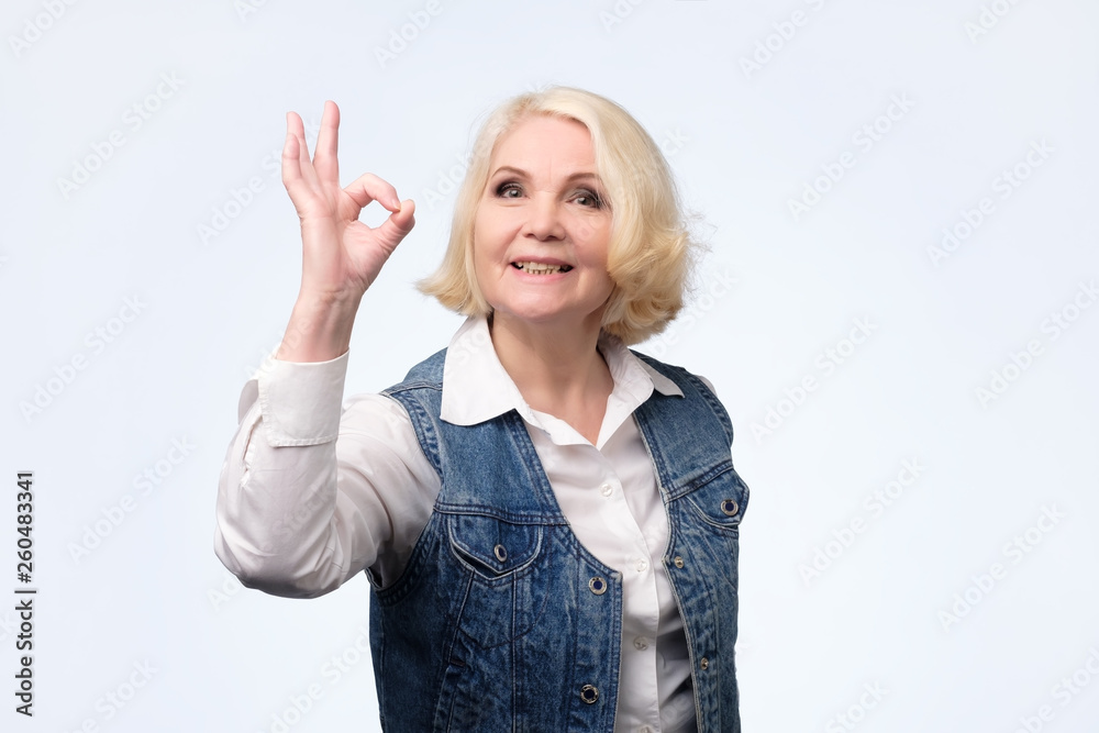Blonde senior woman in casual clothes shows ok sign. Blonde senior woman in casual clothes shows ok sign.