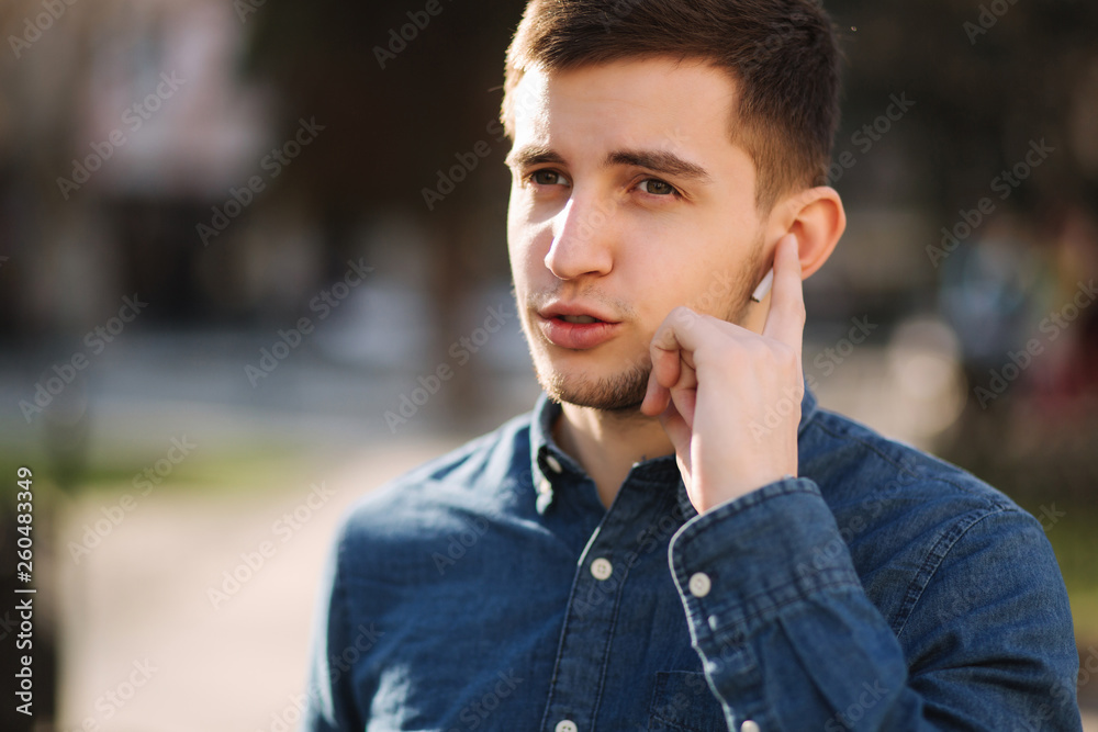 Handsome man put his finger on wireless headphones and speaks. Portrait of man makes conversation by the phone