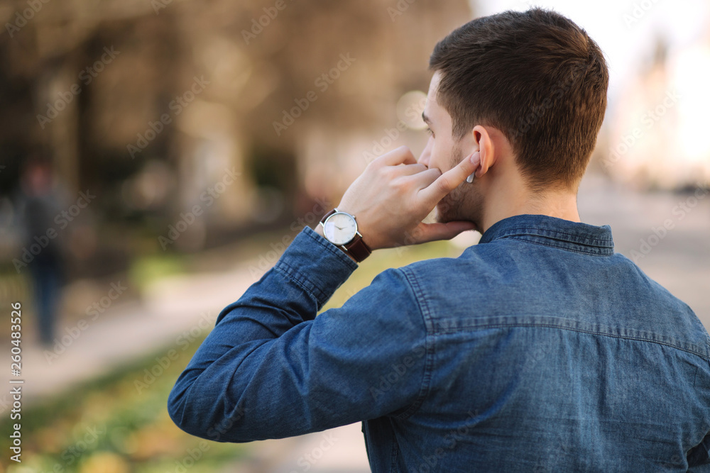 Back view of man usin wireless headphones. Man put his finger on headphone Back view of man usin wireless headphones. Man put his finger on headphone