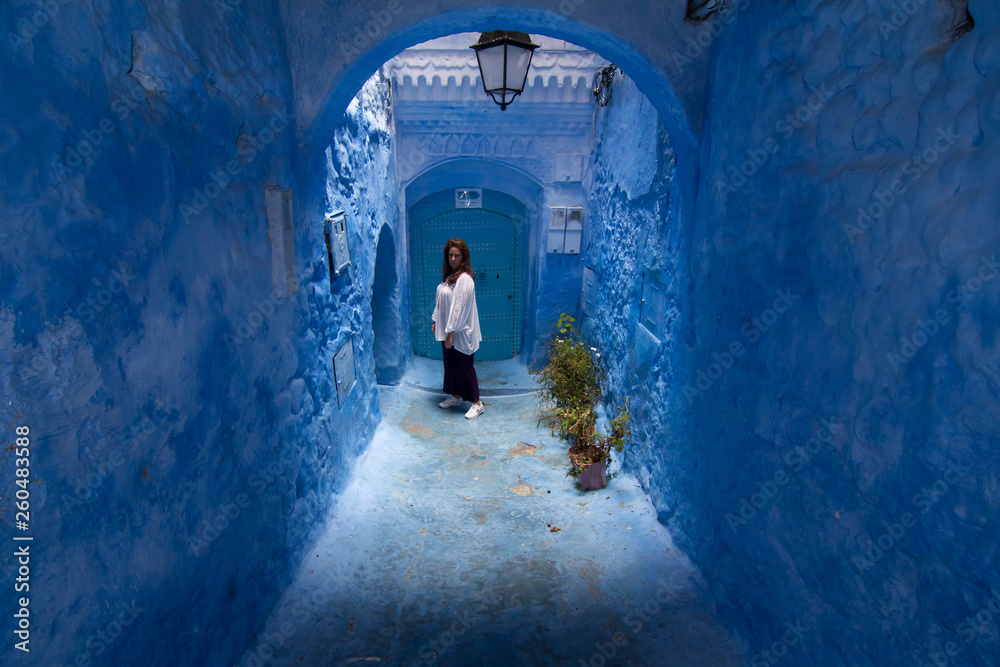 A young woman strolls through the streets of Chefchaouen, the blue town in Morocco, between the walls and the blue arches
