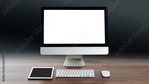 Mock up of a modern desktop computer with blank white screen standing on a wooden table on a dark background.