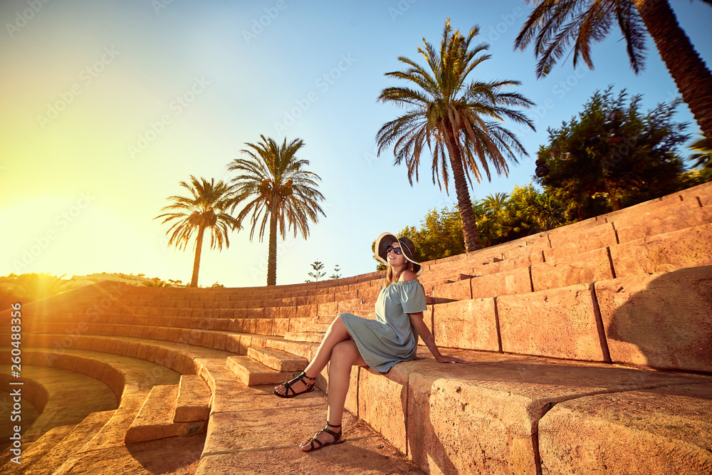 Young beautiful woman in beach hat sitting on the steps of an ancient amphitheater at sunny day in Bodrum, Turkey. Vacation Outdoors Seascape Summer Travel Concept