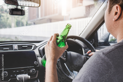 Young asian man drives a car with drunk a bottle of beer behind the wheel of a car photo