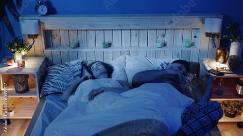 Young couple in bed, snoring woman, man cannot sleep, covering ears with pillow for snore noise, sleeping in bedroom at home. Man is trying to fall asleep while woman is snoring. Health issues problem photo