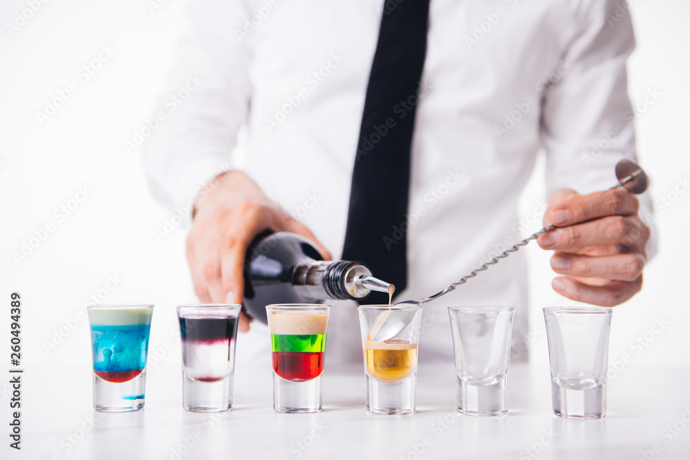 Bartender pours alcoholic drink into small glasses on bar. Colorful cocktails at the bar. Bartender pours alcoholic drink into small glasses on bar. Colorful cocktails at the bar.