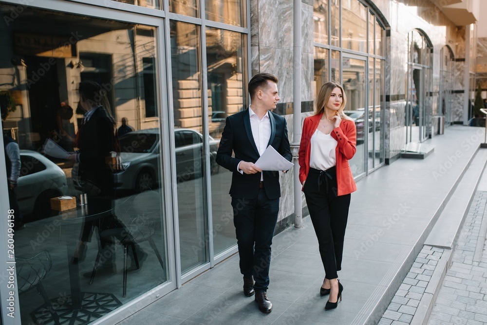 A two young business-people are walking along office building A two young business-people are walking along office building
