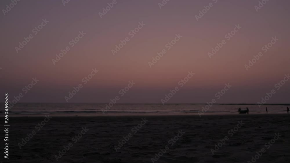 Time lapse of fisherman collecting and wrapping their fishing nets and leave exit frame against the brilliant lit sky at dusk across a vast beach while others play, walk and stroll, speed 2x