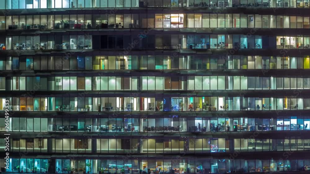 Working evening in glass office building with numerous offices with glass walls and illuminated windows timelapse. People sitting at desks Working evening in glass office building with numerous offices with glass walls and illuminated windows timelapse. People sitting at desks