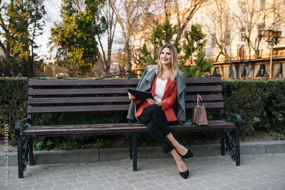 Beautiful woman using tablet computer on an urban bench. Businesswoman wearing suit with trousers and tie, afro hairstyle.