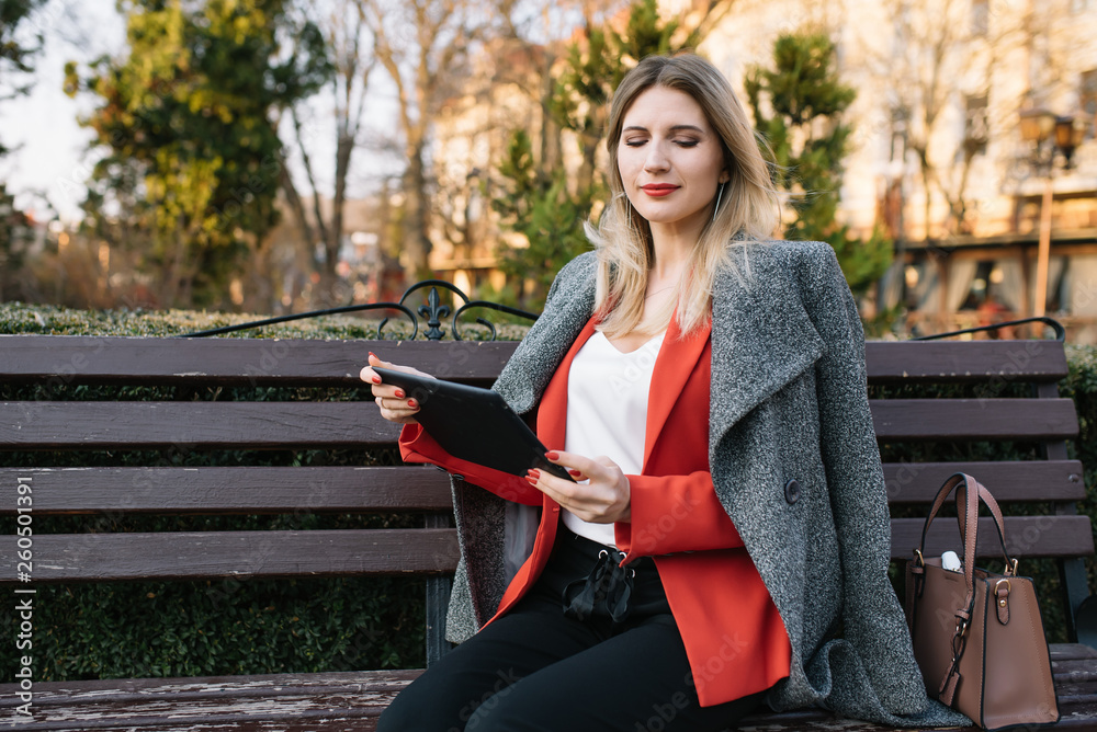 Obraz premium Beautiful woman using tablet computer on an urban bench. Businesswoman wearing suit with trousers and tie, afro hairstyle.
