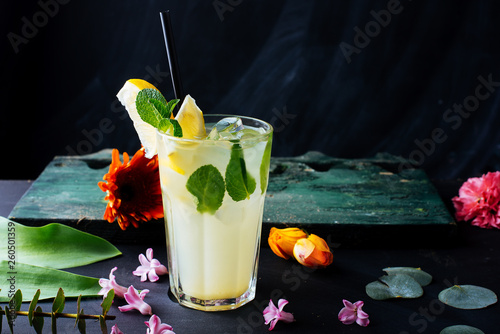 A glass with fresh lemonade on dark table decoratedwith colorful flowers photo