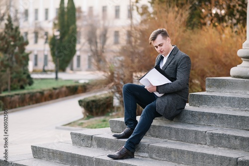 Handsome young businessman working with documents sitting on the stairs outdoor