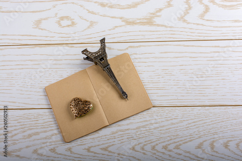 Eiffel tower miniature and a steel heart on a brown notebook on wooden background