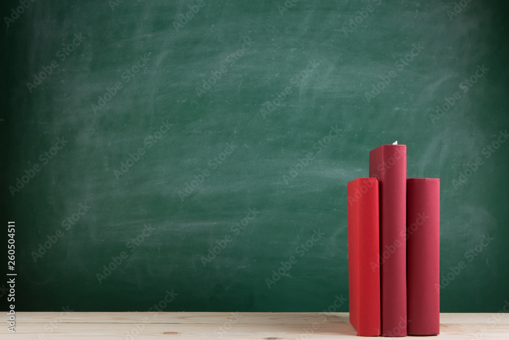Education and reading concept - group of colorful books on the wooden table in the classroom, blackboard background