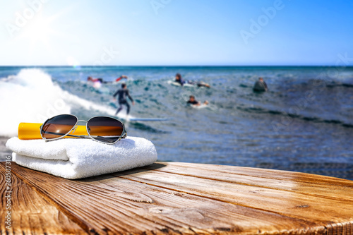 Wooden desk of free space for your decoration. Blurred background of surfers and waves . Blue ocean and white towel decoration. 