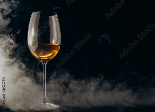a glass of white wine on a black background. the smoke from the hookah envelops the glass. rest, holiday. alcoholic drink closeup. white fog