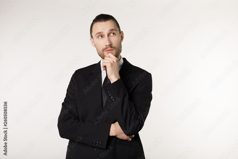 Attractive guy, teacher with stylish hair and beard in black suit holding his chin and thoughtfully looking aside thinking about his future Attractive guy, teacher with stylish hair and beard in black suit holding his chin and thoughtfully looking aside thinking about his future