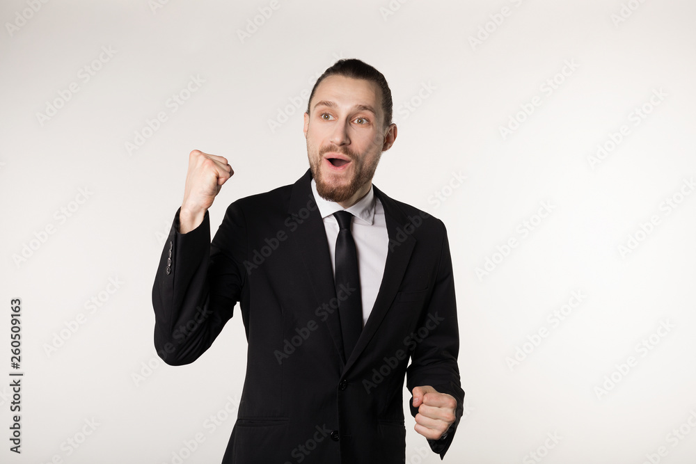 Yes. Winner. Elegant young man are standing and gesturing for the victory on white background in black suit and tie Yes. Winner. Elegant young man are standing and gesturing for the victory on white background in black suit and tie
