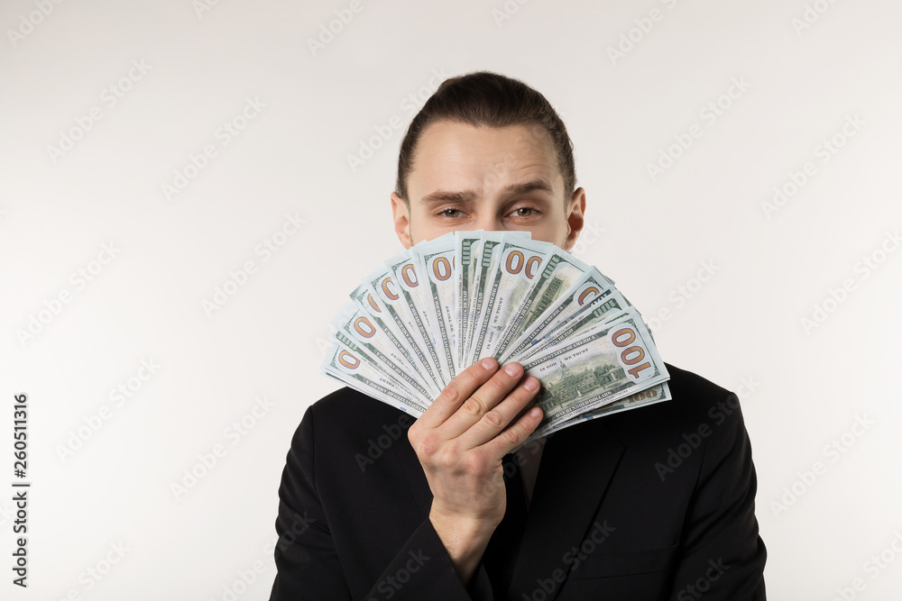 Portrait of handsome businessman in black suit that hides his face behind the money banknotes Portrait of handsome businessman in black suit that hides his face behind the money banknotes