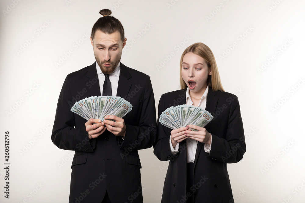 Portrait of couple in black suits shocked holding money banknotes in hands Portrait of couple in black suits shocked holding money banknotes in hands