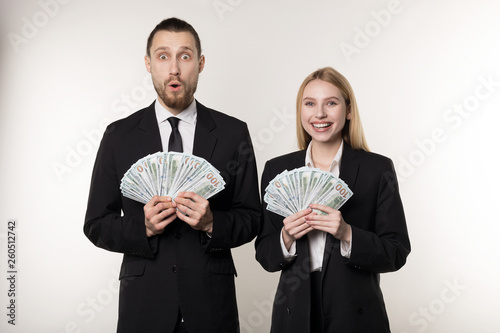 Portrait of couple in black suits shocked holding money banknotes in hands