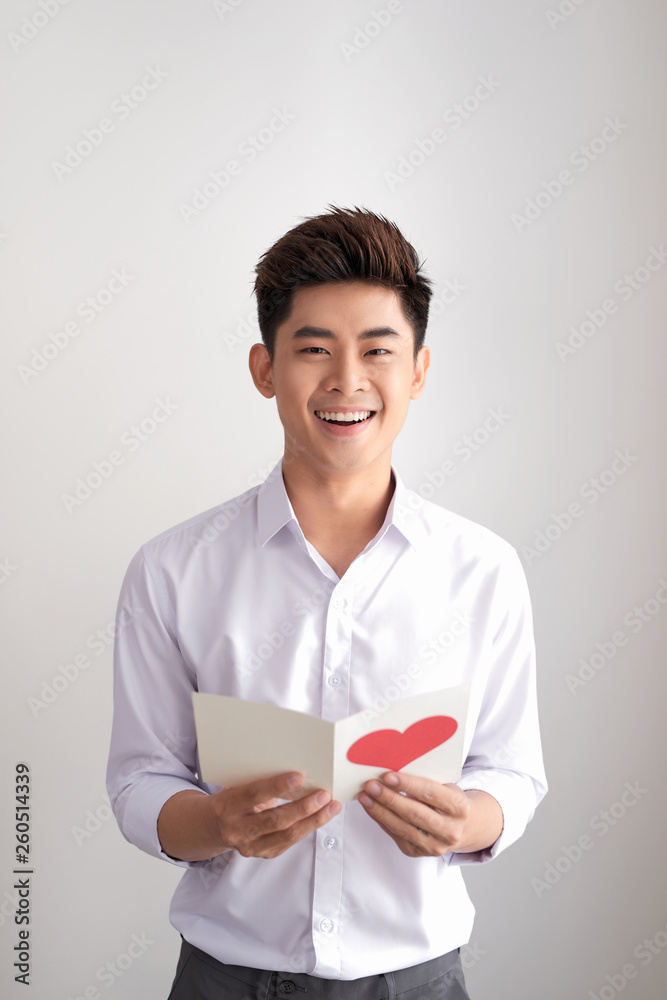 Young handsome asian man reads greeting card with heart shape on white background Young handsome asian man reads greeting card with heart shape on white background