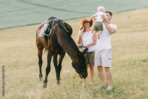 A young family have a fun in the field. Parents and child with a horse
