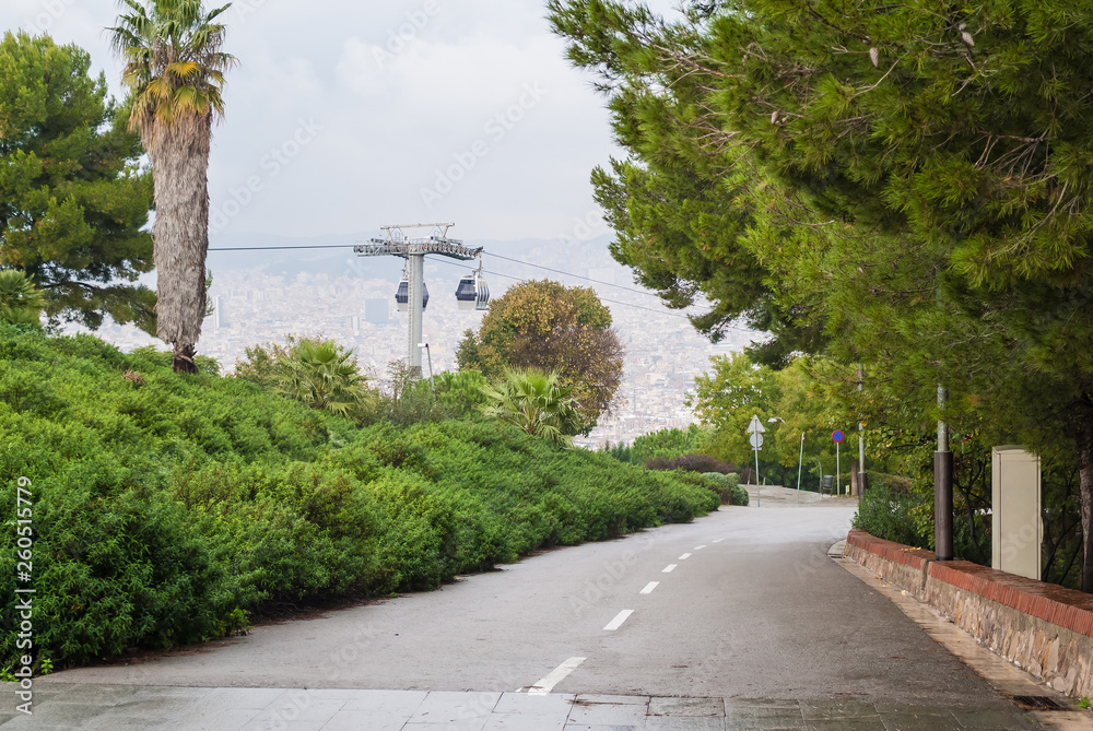 Perspective view of the road on Montjuic mountain, Montjuic Cable Car and Barcelona city from a height in overcast day, Spain