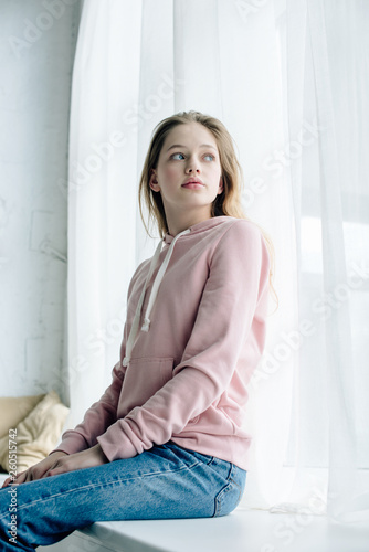 Low angle view of teenager sitting on window sill and looking away