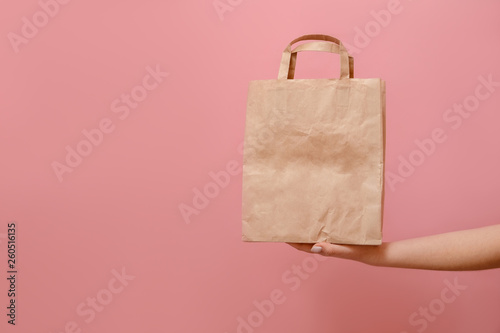 in hands of woman paper bag on pink background