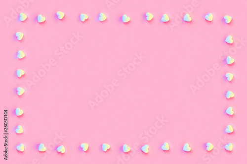 Square frame made of small white sugar candy hearts on a pastel living coral color paper