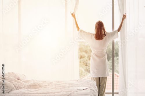 view back woman opening curtains in a white bedroom