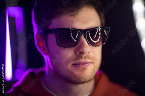 leisure, clubbing and nightlife concept - portrait of smiling young man in sunglasses at dark room over ultra violet neon lights of night club