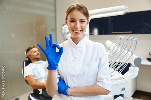 Beautiful happy young woman doctor in medical dentist center showing okay gesture.