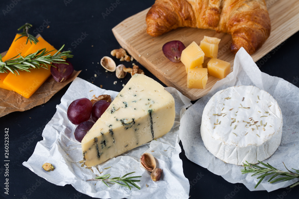 Assorted cheeses: blue cheese with mold, cheddar, parmesan, camembert with grapes, nuts and french croissant.