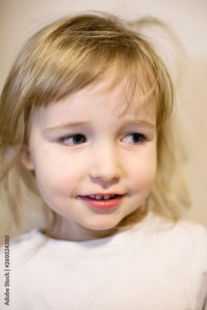 closeup face portrait of cute two years old blonde white girl on wall background