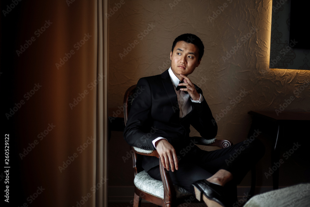 groom holds chin sitting by the window in a luxury hotel groom holds chin sitting by the window in a luxury hotel