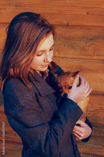 Young Girl Holding A Little Dog Over Wooden Background. Owner And Pet.  Pretty Young Caucasian Girl And Dog. People  Animals Concept.