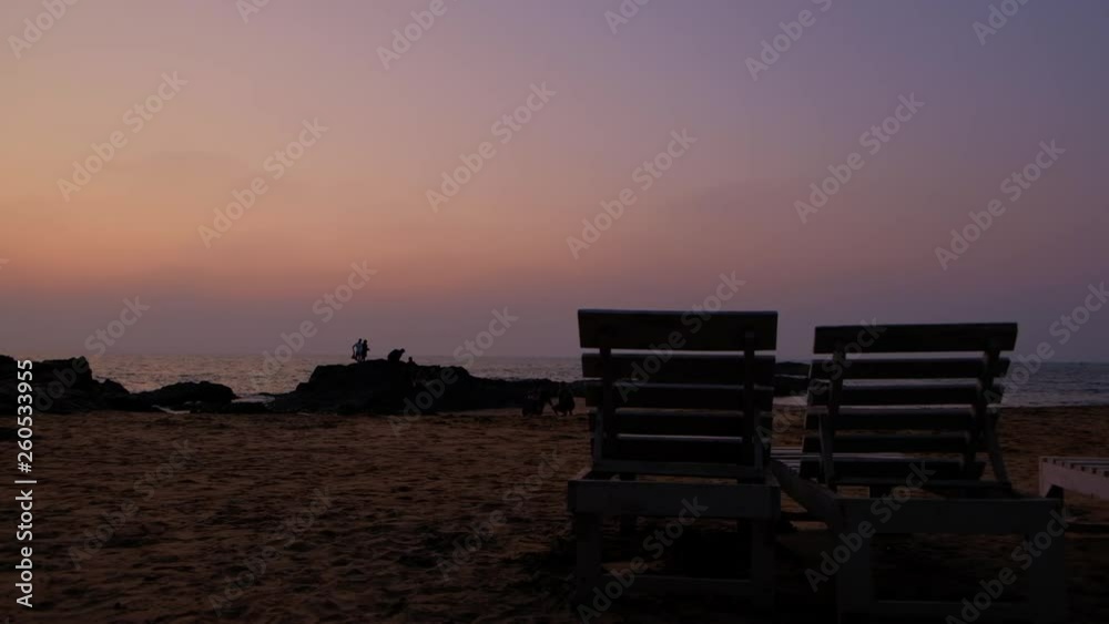 POV of a tourists watching the sun go down with brilliantly lit sky in pink, red, orange and various colors  as seen from resort with view of wooden benches in-between for tourists to relax and calm 