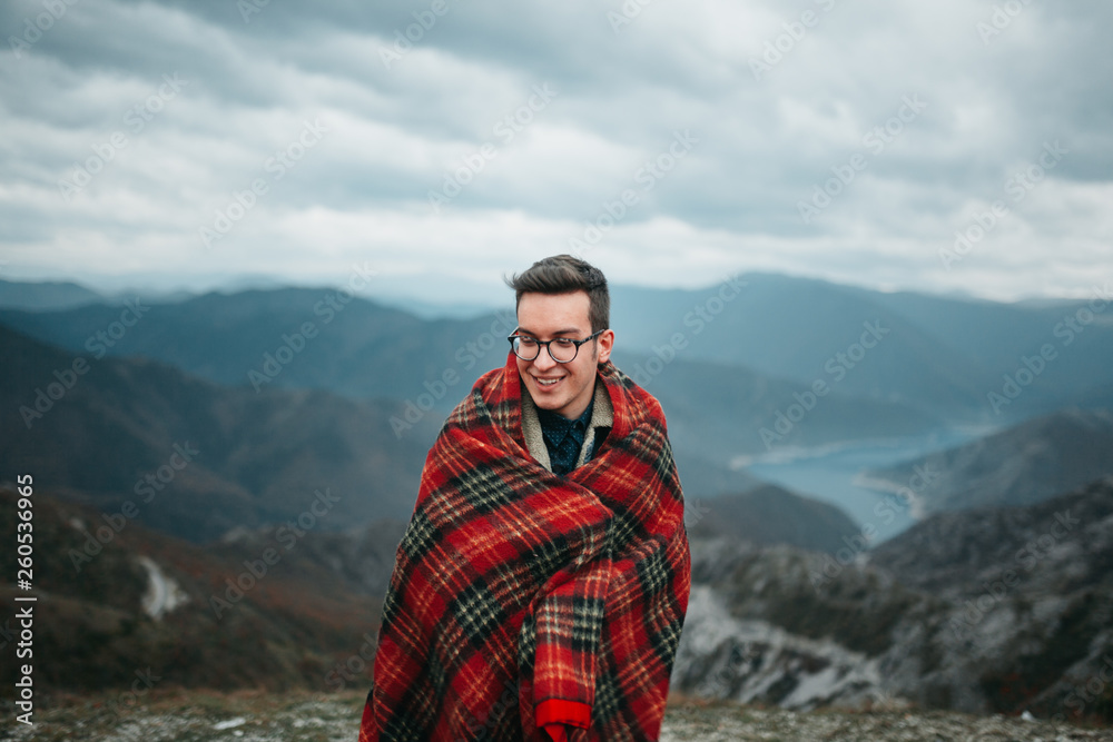 Young Man Wrapped in Checkered Warm Blanket Enjoying on Mountain Top Young Man Wrapped in Checkered Warm Blanket Enjoying on Mountain Top