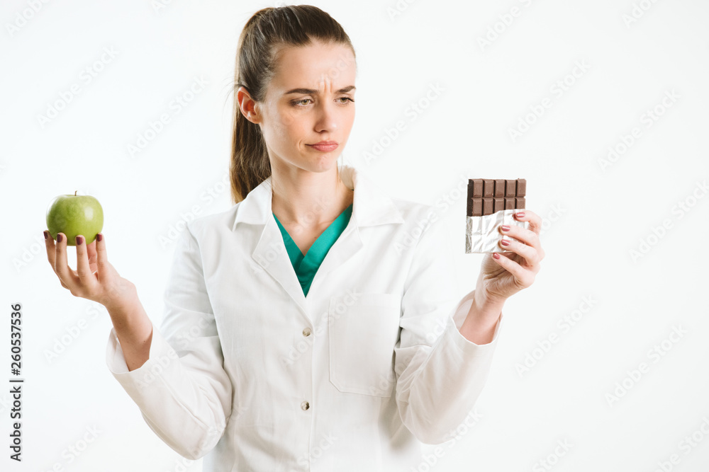 Young nurse holding an apple and a chocolate bar. 